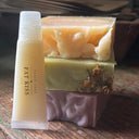 Three bars of soap with a small tube labeled 'Fat Kiss' on a wooden surface.