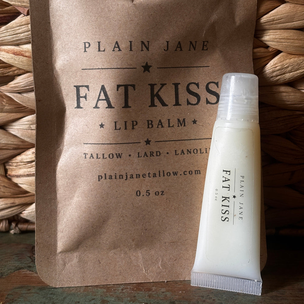 Plain Jane Fat Kiss lip balm packaging on a woven surface