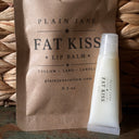 Plain Jane Fat Kiss lip balm packaging on a woven surface