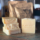 Plain Jane soap bars on a wooden surface with packaging in the background.